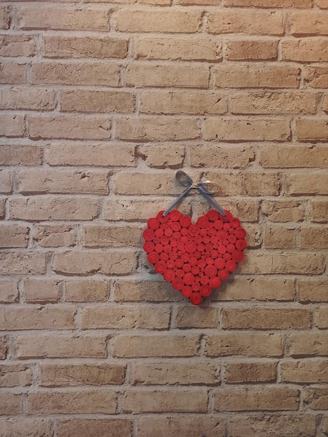 Rotes Herz hängt an einer Ziegelsteinmauer, ein strukturiertes Symbol der Liebe, ein Symbol der Liebenden.