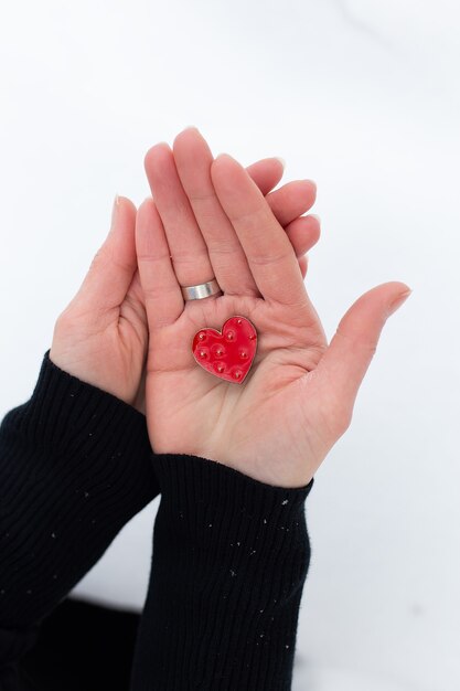 Rotes Herz in den Händen eines Mädchens an einer hellen Wand, es schneit.