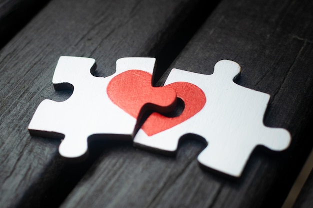 Rotes Herz wird auf die Teile des Holzpuzzles gezeichnet, die nebeneinander auf Holzhintergrund liegen Liebeskonzept St. Valentinstag