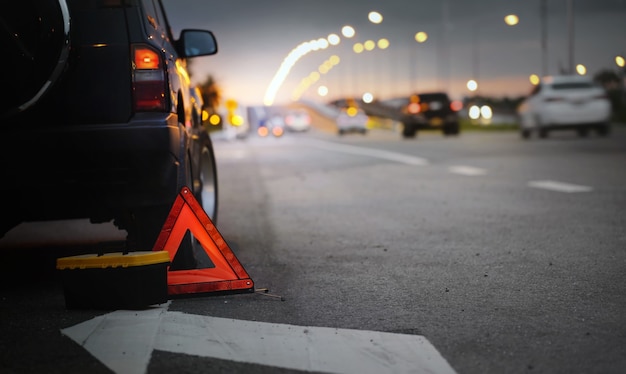 Rotes Notstopp-Schild (rotes Dreieck-Warnschild) und gebrochenes schwarzes SUV-Auto. Selektiver Fokus mit geringer Schärfentiefe.