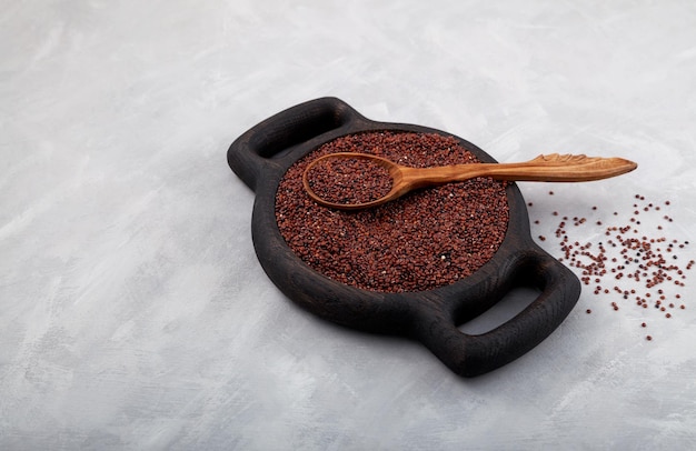 Rotes Quinoa-Korn in Holzplatte und Holzlöffel auf grauem Hintergrund Kopierbereich mit selektivem Fokus