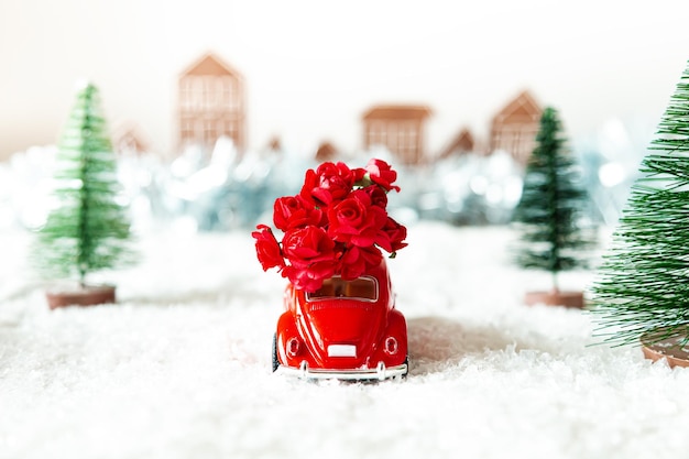 Rotes Retro-Auto mit Blumen in einer Winterlandschaft Blumenlieferung für den Urlaub