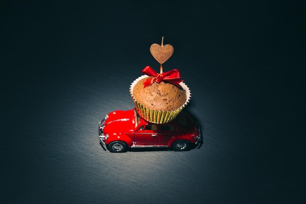 Rotes Retro-Auto trägt einen Schokoladenkuchen mit einer herzförmigen Kerze. Romantische Karte zum Valentinstag. St. Petersburg, Russland – 31. Januar 2022