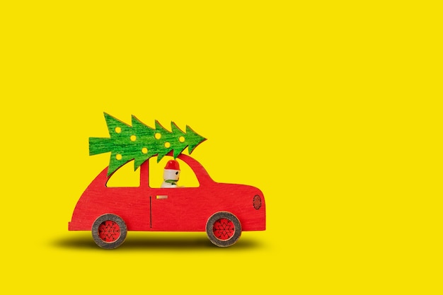 Rotes Spielzeugauto des Holzes mit Weihnachtsbaum auf dem Dach und Schneemann am Rad auf gelbem Hintergrund