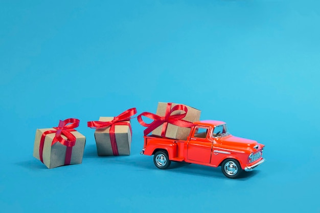 Rotes vintages pickup-truck-auto trägt geschenke einer geschenkbox mit einem roten bogengeschenk auf blauem hintergrund.