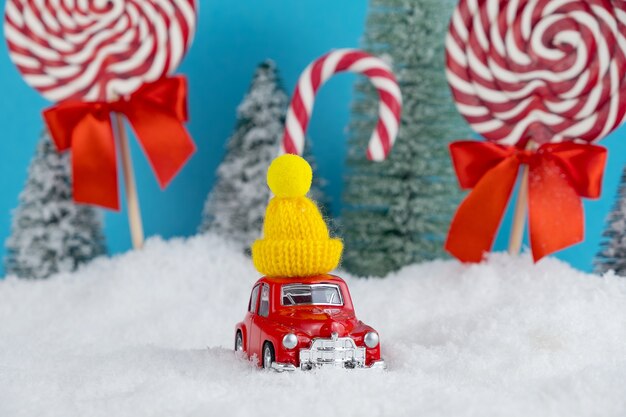 Rotes Weihnachtsmannauto mit in gelber Wintermütze und Weihnachtsbaumwald mit Bonbons und Lutschern