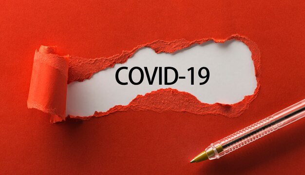 Rotes zerrissenes Papier mit Wort COVID-19 und Stift nah oben