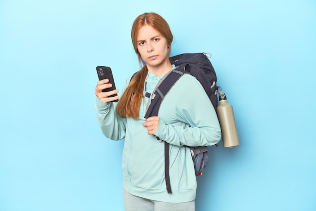 Rothaarige Bergsteigerin mit Abenteuerrucksack im blauen Studio