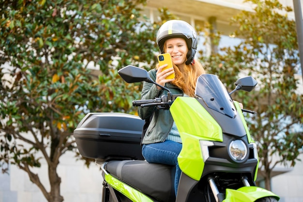 Rothaarige Frau auf ihrem Motorrad mit Smartphone