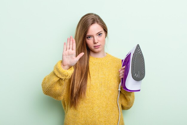 Rothaarige Frau, die ernste offene Handfläche zeigt, die Stoppgeste macht. Eisenkleidungskonzept