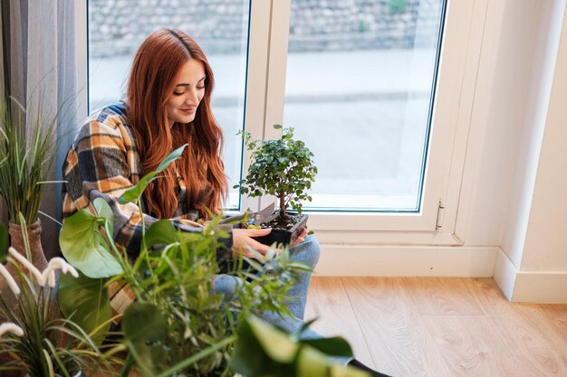 Rothaarige Frau, die sich mit der Gartenschere um ihre Zimmerpflanzen kümmert Konzept Vegetation Pflanzen Gartenarbeit