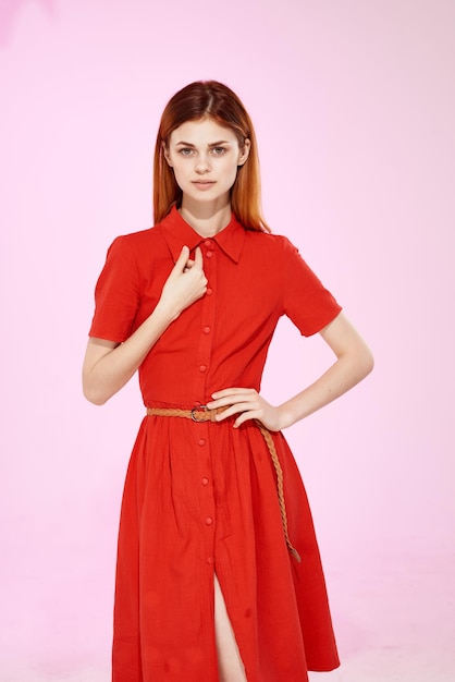 Rothaarige Frau im roten Kleid, das attraktiven Blickrosahintergrund aufwirft