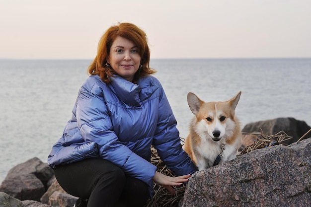 Rothaarige Frau mit einem walisischen Corgi-Hund sitzt auf den Felsen