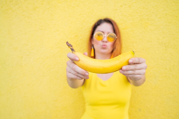 Rothaarige Frau mit Sonnenbrille hält eine Banane auf gelbem Hintergrund