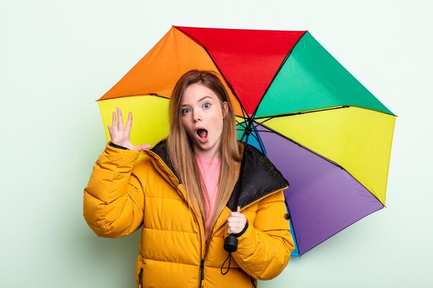 Rothaarige Frau schreit mit den Händen in die Luft. Regenschirmkonzept