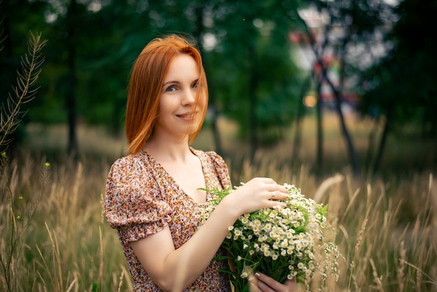 Rothaarige Frau von vierzig Jahren mit einem großen Strauß Wildblumen im Sommer in der Natur