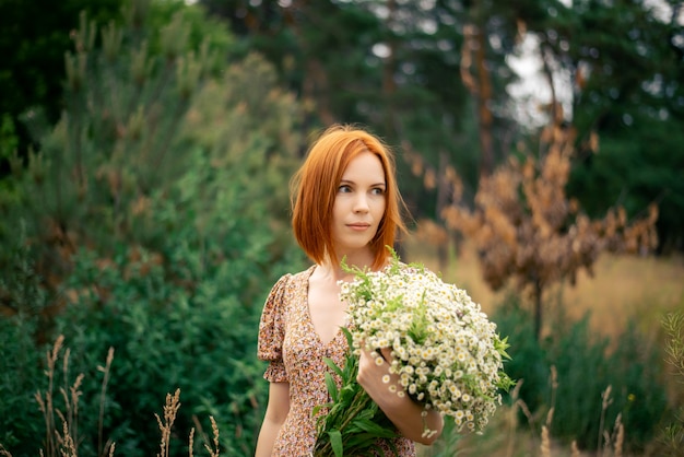 Rothaarige Frau von vierzig Jahren mit einem großen Strauß Wildblumen im Sommer in der Natur