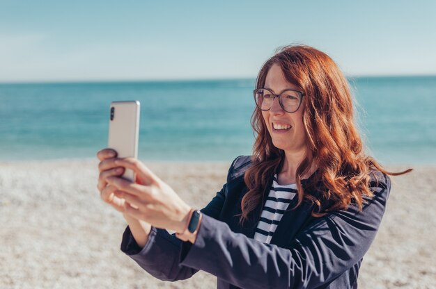 Rothaarige Geschäftsfrau mit Telefon am Meer