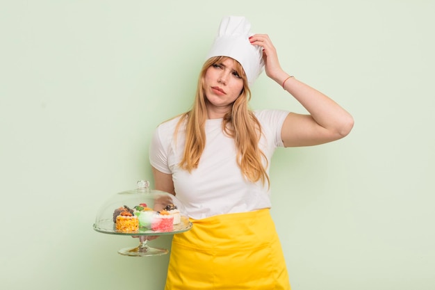 Rothaarige hübsche Frau, die glücklich lächelt und tagträumt oder an hausgemachten Kuchen zweifelt