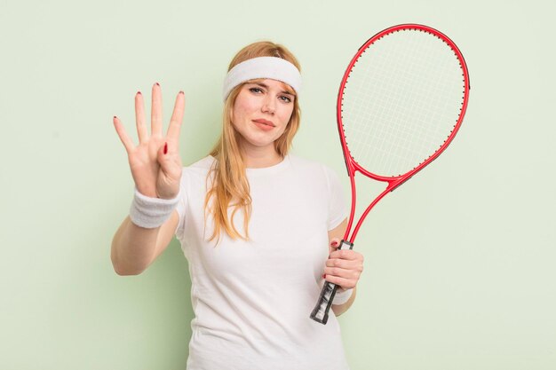 Rothaarige hübsche Frau, die lächelt und freundlich aussieht und das Tenniskonzept Nummer vier zeigt