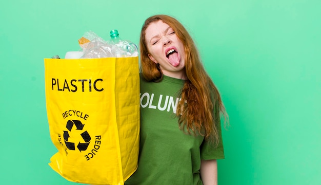 Rothaarige hübsche Frau mit fröhlicher und rebellischer Haltung, die scherzt und die Zunge herausstreckt Recycling-Konzept