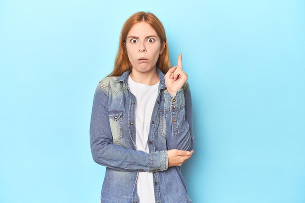 Foto rothaarige junge frau auf blauem hintergrund, die eine tolle idee für kreativität hat