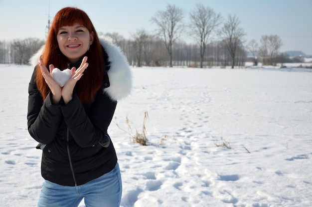 Rothaarige junge Frau, die einen herzförmigen Schneeball in ihren Händen hält