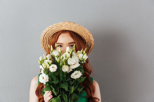 Rothaarige junge Frau, die Gesicht mit Blumen bedeckt.