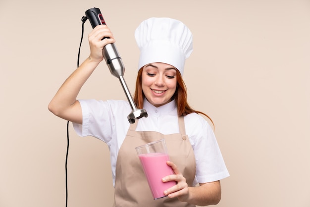 Rothaarige Teenager-Frau mit Handmixer über isolierte Wand