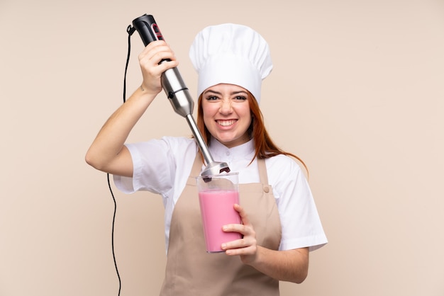 Rothaarige Teenager-Frau mit Handmixer über isolierte Wand