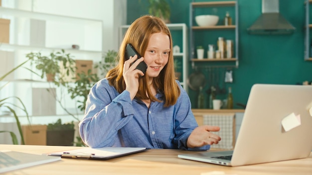 Foto rothaarige teenagerin, die zu hause online studiert und telefoniert