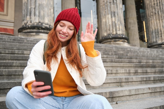 Rothaarige Touristin spricht über Handy-Video-Chats mit Freunden, sagt Hallo und winkt mit der Hand