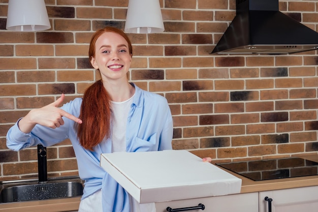 Rothaarige weibliche Holdingbox mit Pizza in der Küche zu Hause