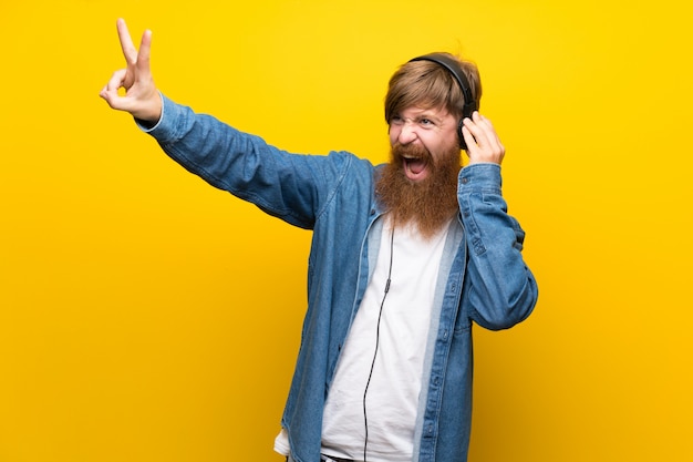 Rothaarigemann mit langem Bart über lokalisierter gelber Wand hörend Musik mit Kopfhörern