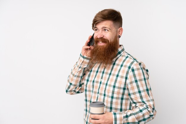 Rothaarigemann mit langem Bart über lokalisierter weißer Wand, die Kaffee hält, um und ein Mobile wegzunehmen