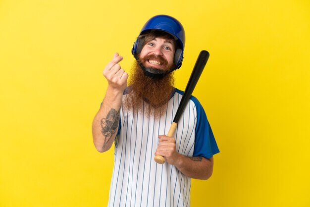 Rothaariger Baseballspieler mit Helm und Schläger isoliert auf gelbem Hintergrund, der Geldgeste macht