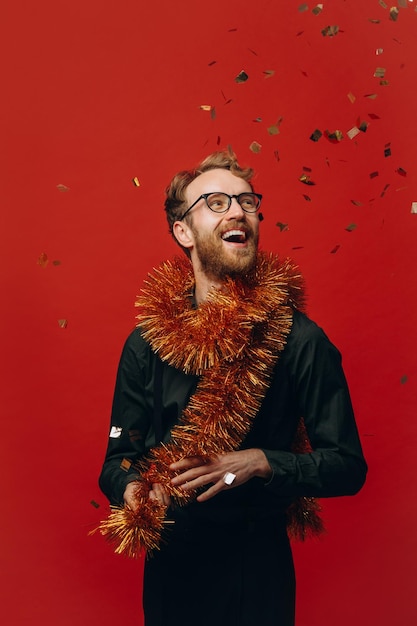 Rothaariger fröhlicher Mann mit Brille und goldener Boa auf der Neujahrsparty mit Konfetti Studiofoto