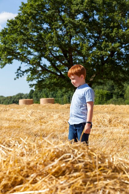 Rothaariger Junge neben einem goldenen Strohhaufen auf einem Feld