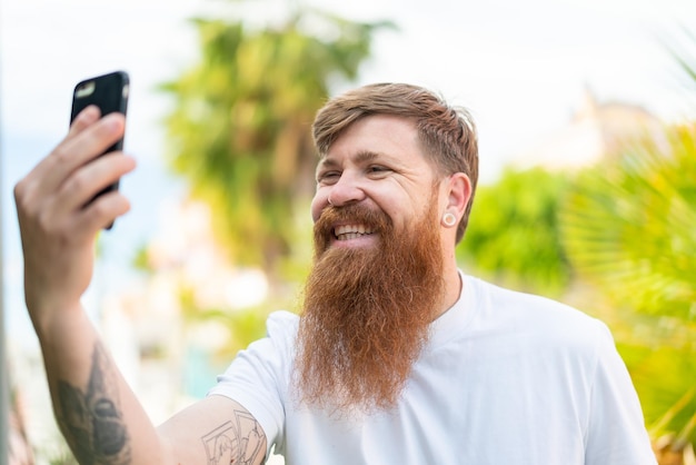 Rothaariger Mann mit Bart, der ein Selfie mit Handy macht