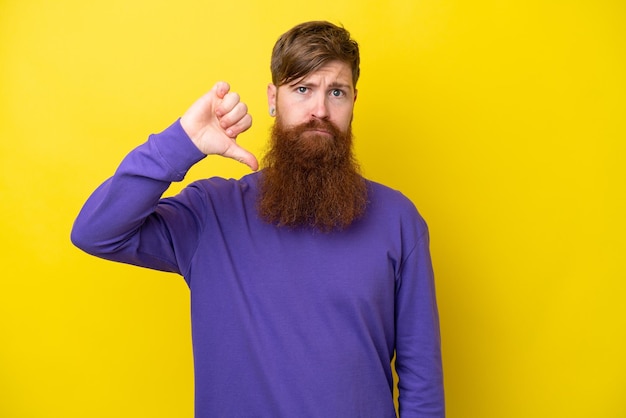 Rothaariger Mann mit Bart isoliert auf gelbem Hintergrund, der den Daumen nach unten mit negativem Ausdruck zeigt