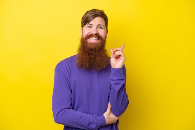 Rothaariger Mann mit Bart isoliert auf gelbem Hintergrund glücklich und nach oben zeigend