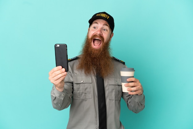 Rothaariger Sicherheitsmann isoliert auf weißem Hintergrund mit Kaffee zum Mitnehmen und einem Handy