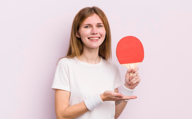 Rothaariges hübsches Mädchen, das fröhlich lächelt und sich glücklich fühlt und ein Ping-Pong-Konzept zeigt