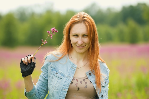 Rothaariges Mädchen hält eine Blume in der Hand auf der Wiese, Sommer