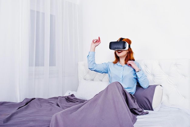 Rothaariges Mädchen im Bett mit VR-Brille im Studiozimmer