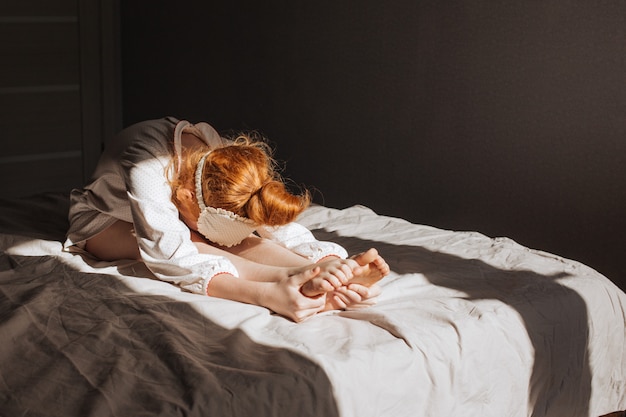 Rothaariges Mädchen im Pyjama, das am frühen Morgen Yoga auf dem Bett macht