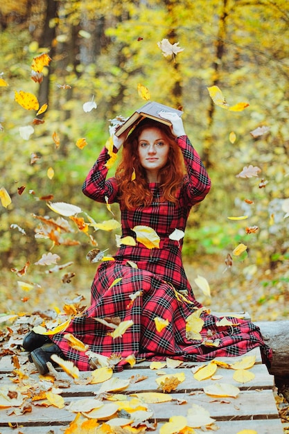 Rothaariges Mädchen im roten Kleid, Hut, der im Herbstwald spaziert. glücklicher lebensstil. Herbstsaison. Gelbe Blätter