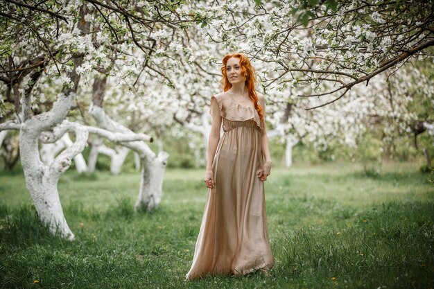 Rothaariges Mädchen in einem beigen Kleid im Garten