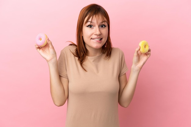 Rothaariges Mädchen isoliert auf rosa Hintergrund mit Donuts