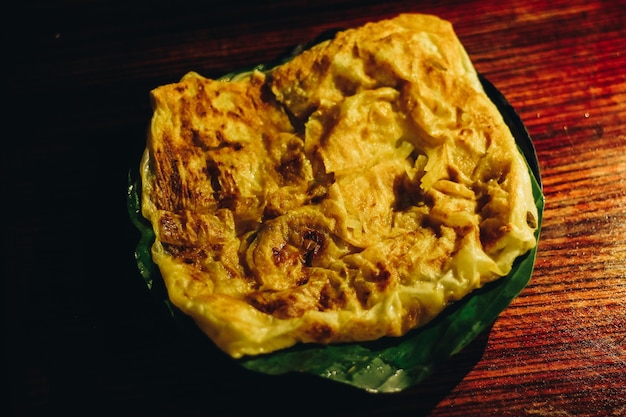 Roti Canai oder Canai-Brot oder Parata-Brot oder Prata-Brot mit Curry-Sauce auf der Bananenblattplatte isoliert auf Holzhintergrund mit dunklem Hintergrund und Scheinwerfer